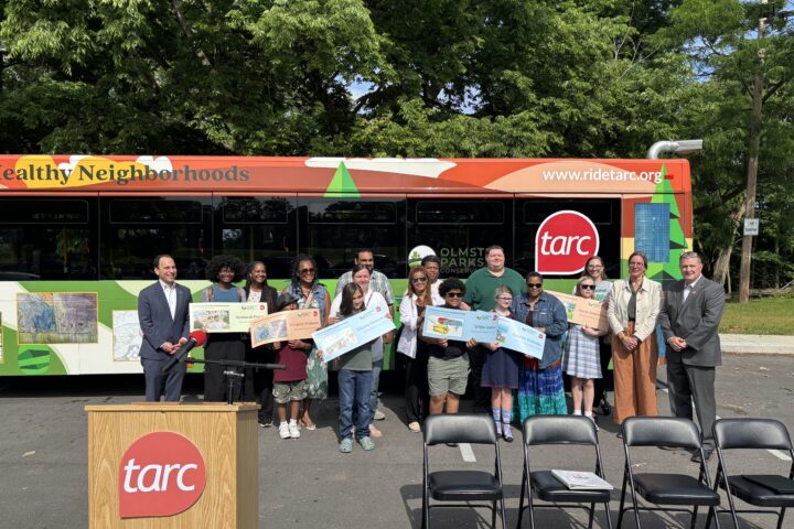 A group of people including the Mayor posing in front of a TARC bus holding signs and awards, with a podium labeled 